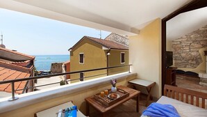 Un balcón con vistas al mar, una mesa de madera con cosas para el desayuno, una cama y un muro de piedra.