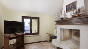 Una sala de estar con una televisión sobre un mueble de madera, una chimenea de piedra y un ventanal con vistas.