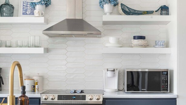 A modern kitchen with a white island, dark cabinets, a stainless steel range hood, and a microwave.