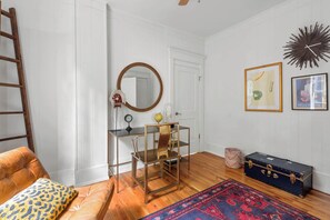 Une pièce avec un plancher en bois, un canapé en cuir, une table en verre avec des chaises, un miroir, un globe terrestre, une horloge, une valise et des œuvres d’art encadrées accrochées au mur.
