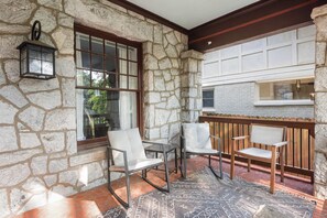 Une terrasse dallée de pierres, avec trois chaises et une table, une lanterne et une fenêtre donnant sur un paysage verdoyant.