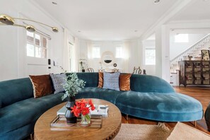 A spacious living room with a large teal sectional sofa, a wooden coffee table, and a decorative mirror above it. - Edgy Overlook (Atlanta)