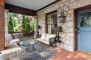 Un porche de paredes de piedra con una puerta azul, muebles de mimbre y una mesa de vidrio.