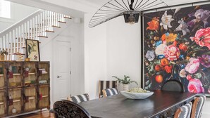 A dining area with a dark wooden table, patterned chairs, a floral mural, and a staircase with white railings. - Edgy Overlook (Atlanta)