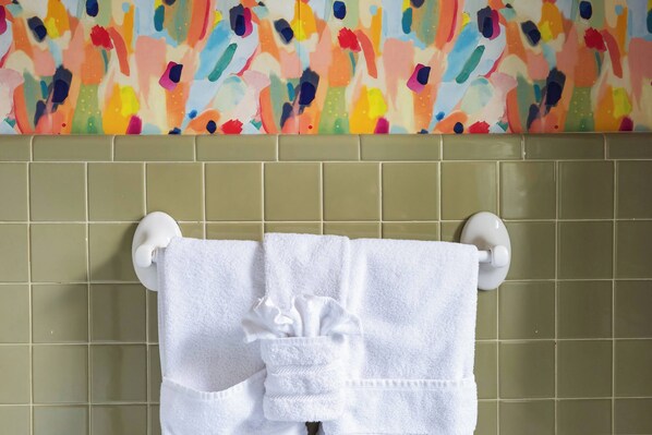 Un baño con paredes de azulejos verdes, un mural abstracto colorido y toallas blancas colgadas en un perchero.