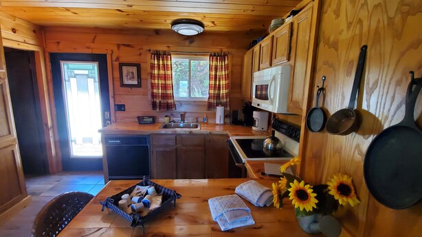 A cozy cabin interior with wooden walls, a kitchen area including a stove, sink, and microwave, and a dining area with a table set for two. - Majestic Peak - Mountain Views and Lake Access (Butler)