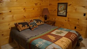 A wooden cabin room with a bed, pillows, a lamp, and a framed poster on the wall. - Majestic Peak - Mountain Views and Lake Access (Butler)