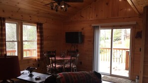 A cozy cabin interior with a dining area, a television, and a large sliding glass door leading to an outdoor deck. - Majestic Peak - Mountain Views and Lake Access (Butler)