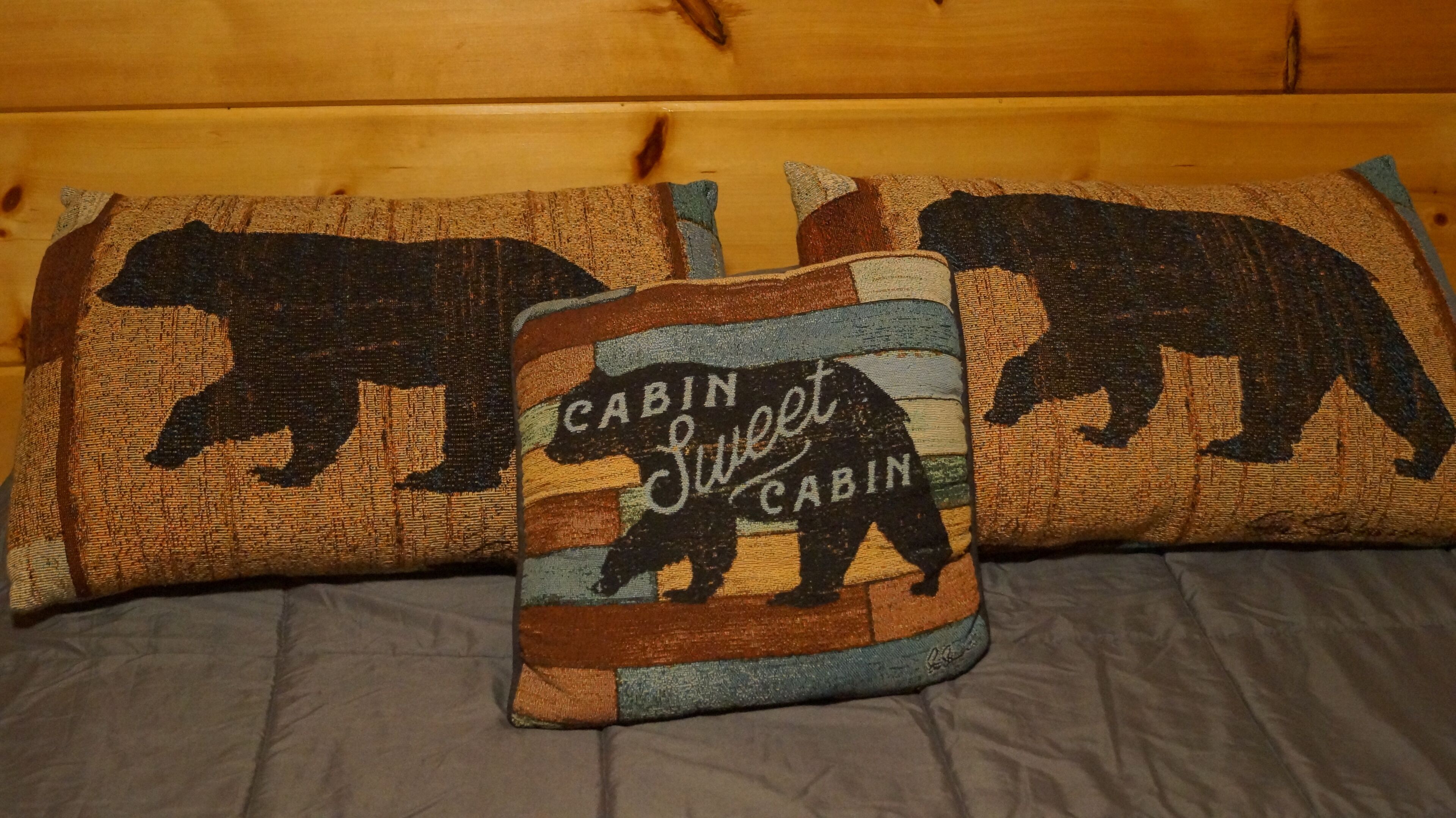 Un lit avec deux oreillers ornés de motifs d’ours et portant l’inscription « Cabin Sweet Cabin ».