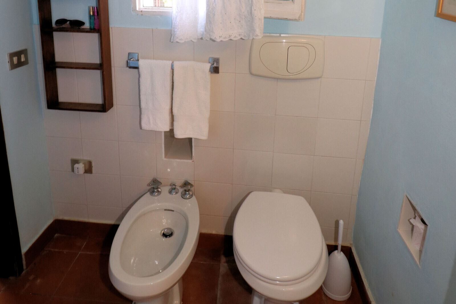 A bathroom with a bidet, toilet, and a shelf with toiletries.