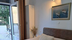Una camera da letto con un letto grande, un quadro con delle barche, una pianta in vaso e vista su uno spazio esterno tramite una porta scorrevole.