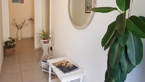 Un corridoio con una porta bianca, un tavolo bianco con un libro, uno specchio grande e una pianta in vaso.