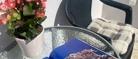A glass table with a book titled 'Dubrovnik' and a potted plant with red flowers.