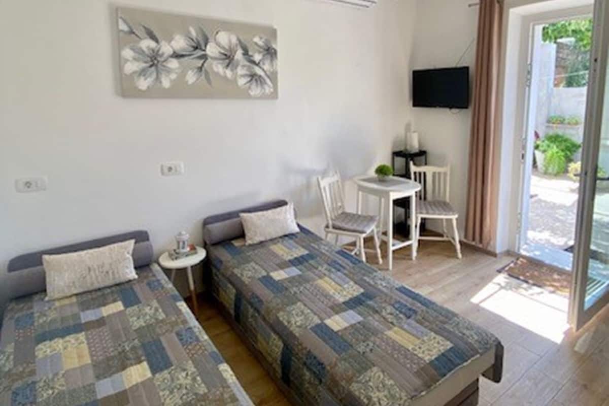 Una habitación con dos camas, una mesa pequeña con sillas, un televisor de pantalla plana y un ventanal grande con cortinas.