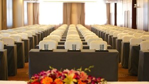 Ett konferensrum med rader av stolar och ett bord längst fram, dekorerat med en blomsterarrangemang.
