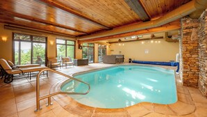 Una piscina interior con vigas de madera, paredes de piedra y un área de descanso con sillas y una mesa.