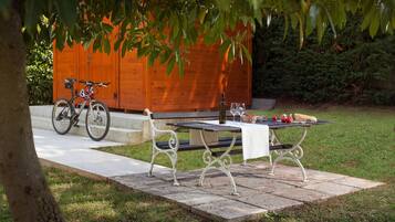 A picnic setup with a table, benches, and a bicycle in a garden area with a wooden structure in the background.