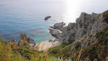 A coastal landscape with rocky cliffs, a beach, and a clear view of the sea.