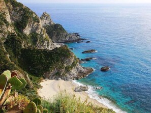 A coastal landscape with a beach, rocky cliffs, and cacti. - Casa Lampedusa, for 2 people, with sea view, shared pool and access to the beach (Capo Vaticano Ricadi)