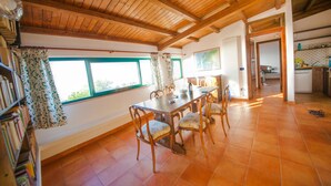 A dining area with a wooden table and chairs, large windows with curtains, and a view of the outdoors. - Casa Lampedusa, for 2 people, with sea view, shared pool and access to the beach (Capo Vaticano Ricadi)