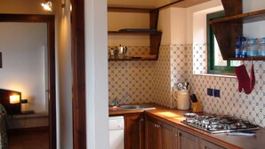 A kitchen with wooden cabinets, a gas stove, a sink, and a window with a view of the outside. - Casa Lampedusa, for 2 people, with sea view, shared pool and access to the beach (Capo Vaticano Ricadi)