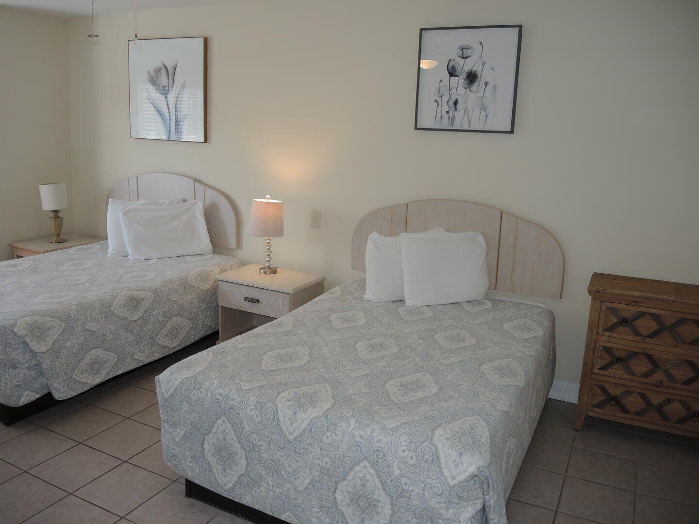 Ein Hotelzimmer mit zwei Betten, jeweils mit Kopfteil, einem Nachttisch mit Lampe und einem Holzbeistelltisch.