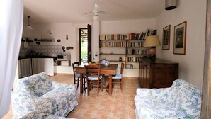 Ein gemütliches Wohnzimmer mit floralen Sofas, einem Holzespeisetisch und einem Bücherregal voller Bücher.