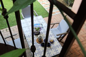 Eine Terrasse mit Tisch für zwei Personen, umgeben von Stühlen, einem kleinen Gartenbereich und einem Pflasterweg.