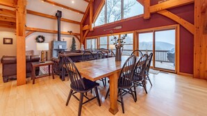 Un vaste espace dédié à la salle à manger, avec une grande table et des chaises en bois, une cheminée et de grandes fenêtres offrant une vue sur l’extérieur.