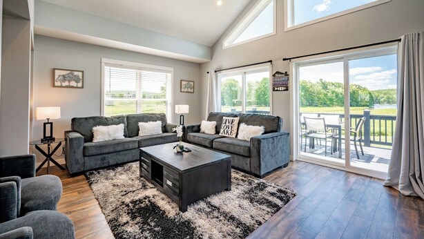 A spacious living room with a large sofa set, a coffee table, and a view of the outdoors through a sliding glass door.
