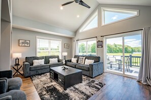 A spacious living room with a large sofa set, a coffee table, and a view of the outdoors through a sliding glass door. - Scenic Dog Friendly Stay w/ Hot Tub & Fire Pit (Swanton)