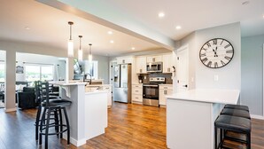 A modern kitchen with white cabinets, a large island with stools, stainless steel appliances, and a wall clock.