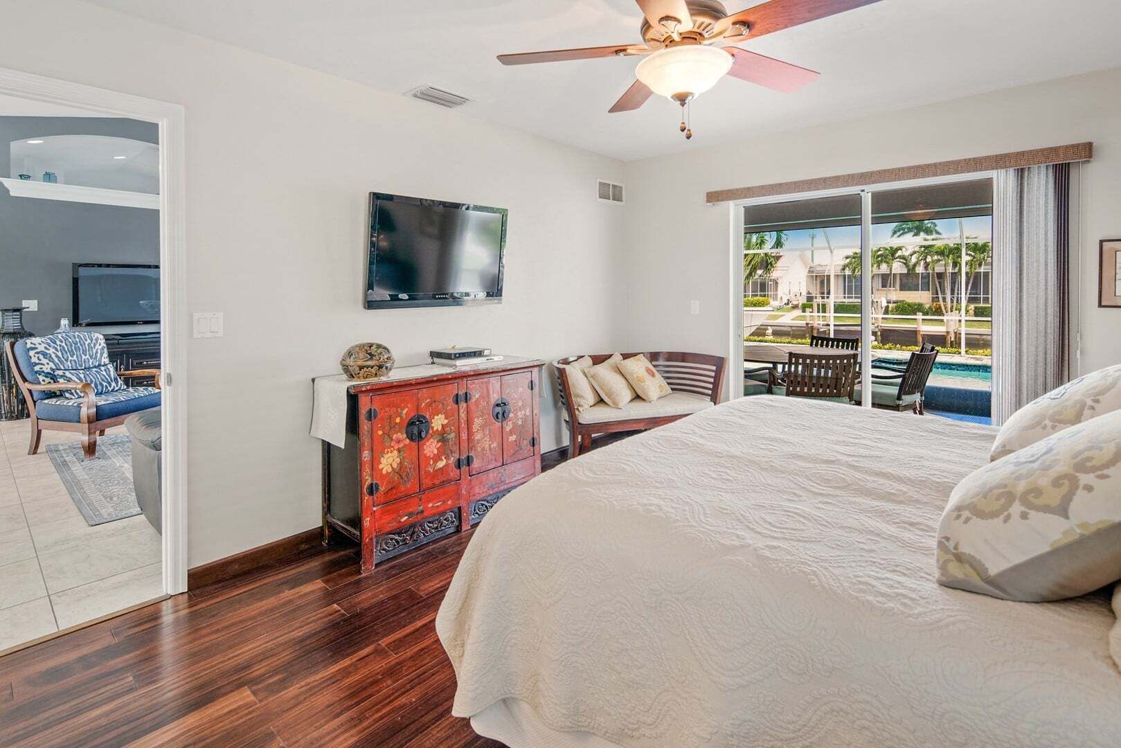 A hotel room with a bed, a television, a wooden cabinet, and a view of a pool.