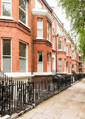 A row of red brick townhouses with white window frames, black iron railings, and a paved sidewalk. - The Luxury 'Treehouse' One bed Little Venice- by Out of Office Lifestyle (London)