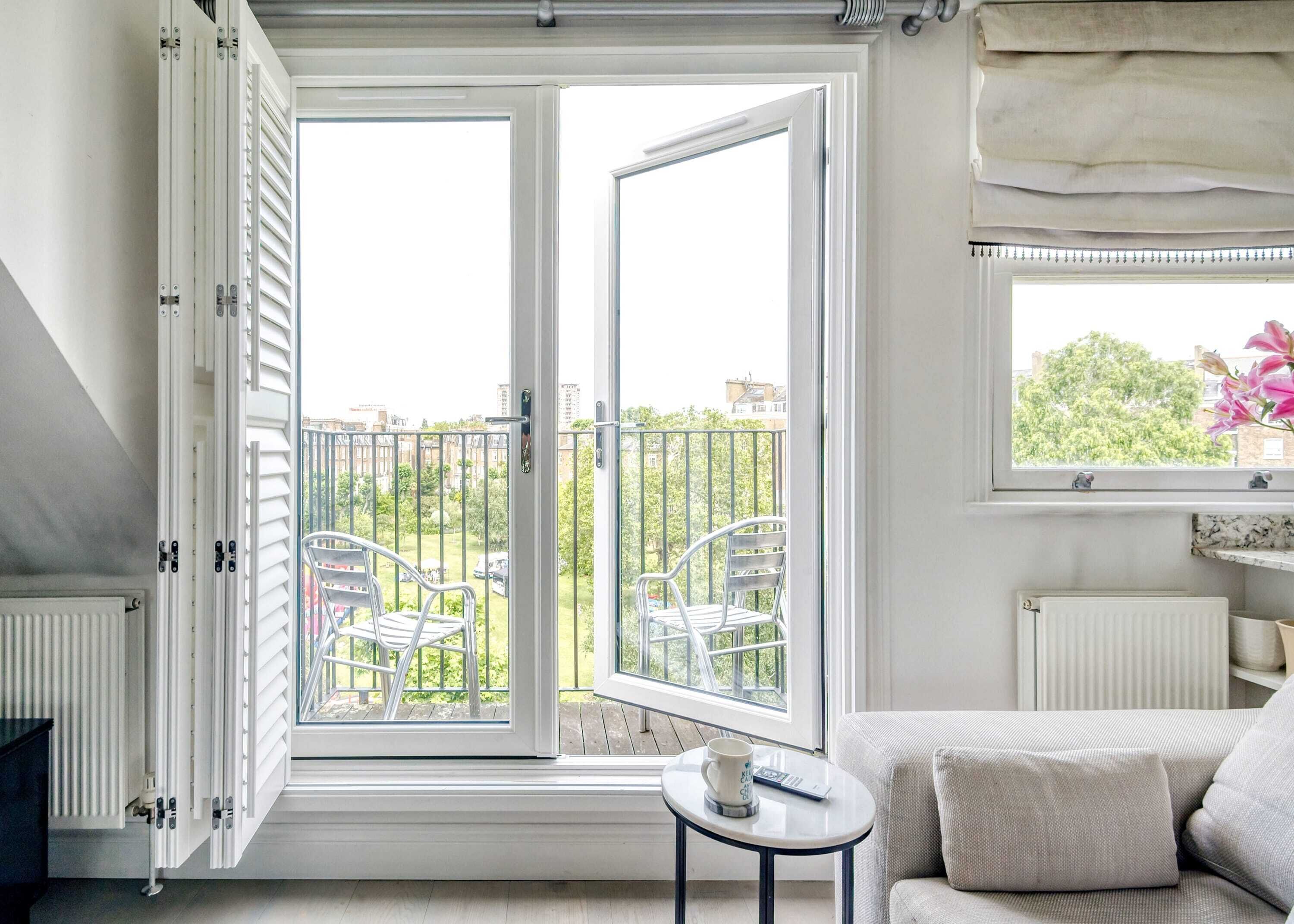 A room with a large open window, a sofa, a small table with a remote control, and a radiator.