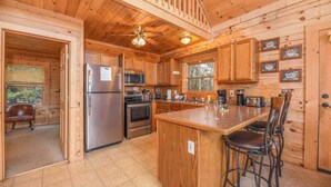 Una cabaña de madera con cocina equipada con refrigerador, microondas y estufa. Hay un comedor con mesa y sillas.