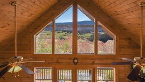 Interior de madera con techo alto, ventanas amplias que ofrecen vistas al paisaje y ventiladores de techo.
