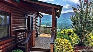Una cabaña de madera con un porche, una mesa pequeña y sillas, y vistas a un paisaje montañoso.