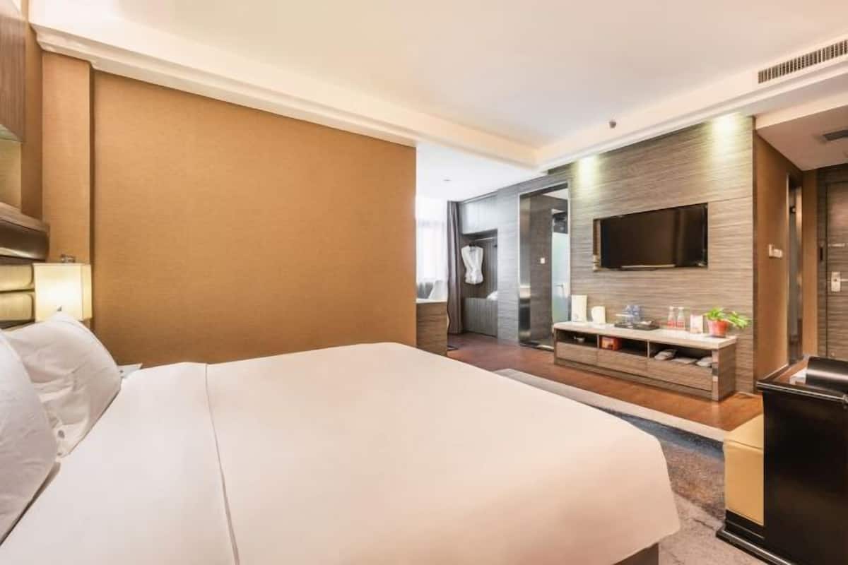A hotel room with a large bed, a flat-screen TV mounted on the wall, a small console table with a mirror, and a door leading to a bathroom.