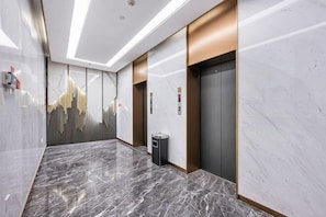 A modern hallway with marble flooring, elevators, and a trash bin. - Jindi Mingting Hotel (Lanzhou)