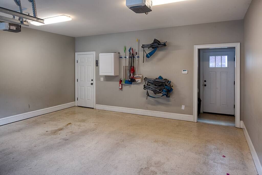 A clean, well-lit garage with a white door, a white cabinet, and various tools and equipment hanging on the wall.
