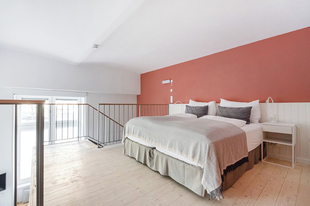 Un dormitorio con cama, mesitas de noche, una ventana y una escalera.