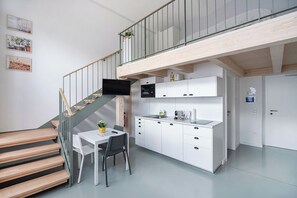 Une cuisine moderne avec des meubles blancs, un coin repas comprenant une table et des chaises, et un escalier menant à un balcon.