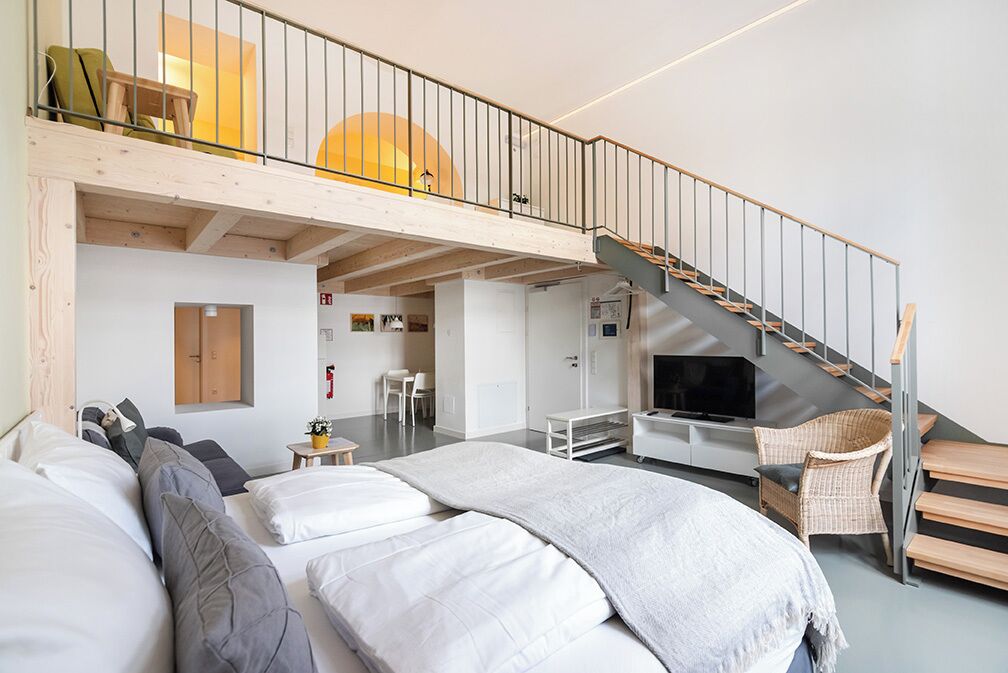Ett modernt hotellrum med en öppen sovplats på ett övre plan, en trappa och en tv.
