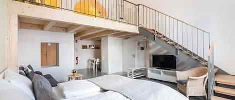 Ein modernes Hotelzimmer mit Schlafbereich auf Podest, einer Treppe und einem Fernseher.