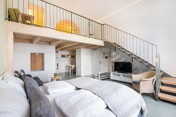 Une chambre d’hôtel moderne avec un espace nuit en mezzanine, un escalier et un téléviseur.