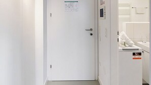 En smal hall med ett träpanelat tak, en vit dörr med en anslagstavla och en vit vägg.