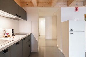 Eine moderne Küche mit grauen Schränken, einer weißen Arbeitsplatte und einem eingebauten Herd. Rechts befindet sich ein weißes Kühlschrank, und eine Tür führt in einen anderen Raum.