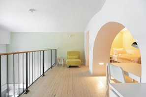 Un intérieur moderne avec un plancher en bois, un fauteuil jaune, une table blanche et un lit doté d’une tête de lit blanche.
