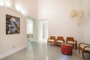A modern interior with a reception area, wooden chairs, a red ottoman, and a wall-mounted light fixture.